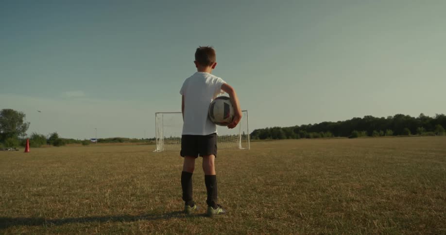 A boy is holding a soccer ball and standing in a field