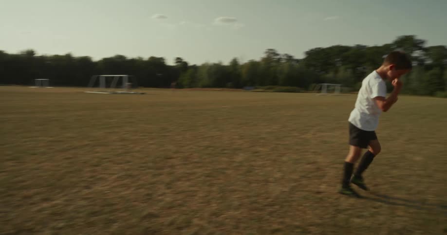 Boy kicking a ball on a soccer field and celebrating happily
