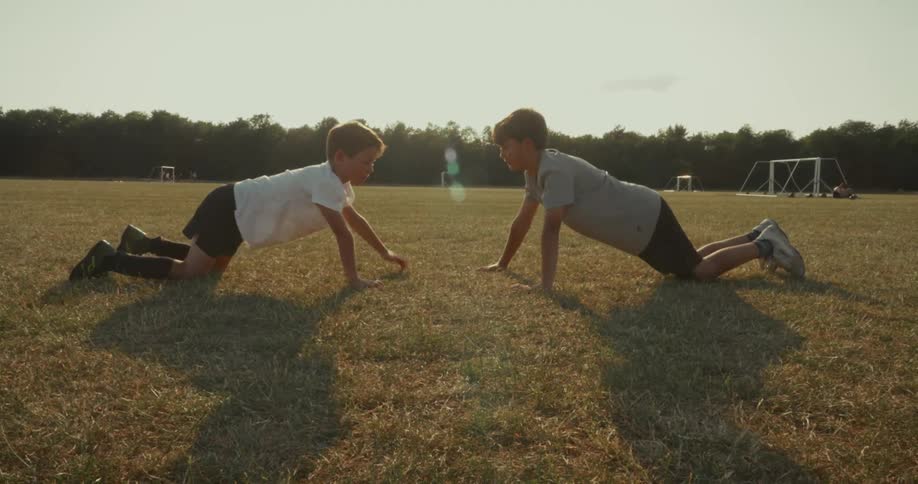 Two boys doing pushups in a field and touching hands with each other
