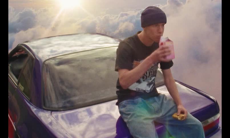 Man eating bread and drinking yogurt while sitting on the hood of a car trunk floating in the sky with clouds