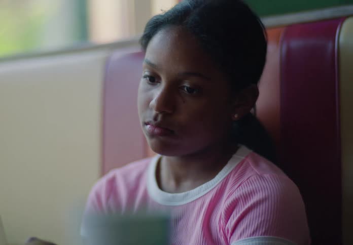 A teenage girl sits in a restaurant at midday with a burger and fries served in front of her looking sad
