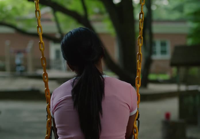 A girl sits alone on a swing facing away in a quiet playground