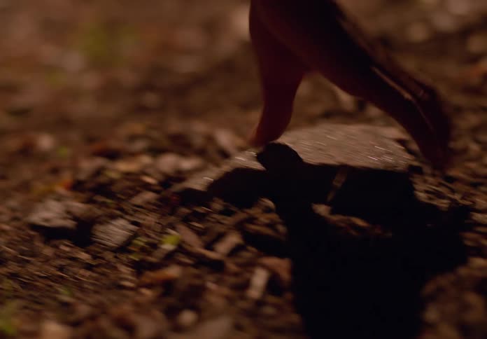 A hand reaches down to pick up a rock from a dimly lit textured ground