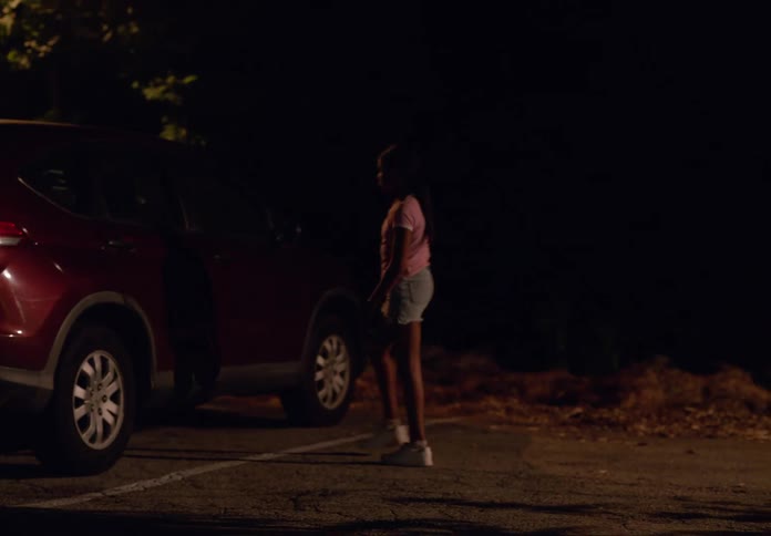 A child crouches beside a parked car at night on a dimly lit street