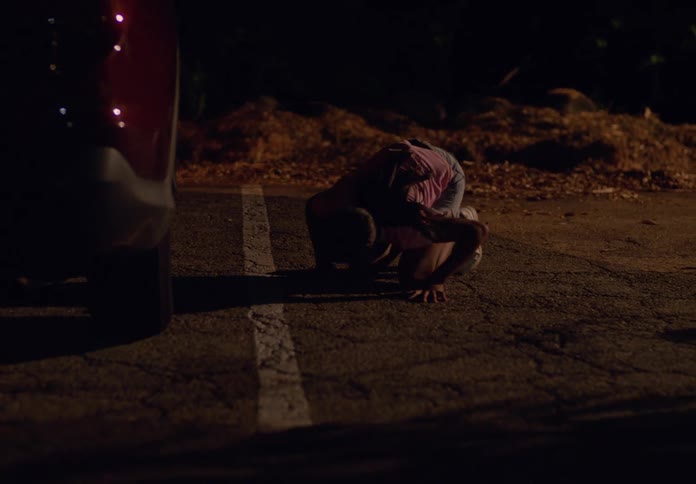 A teenage girl looks under a car finds nothing and continues walking down the street at night