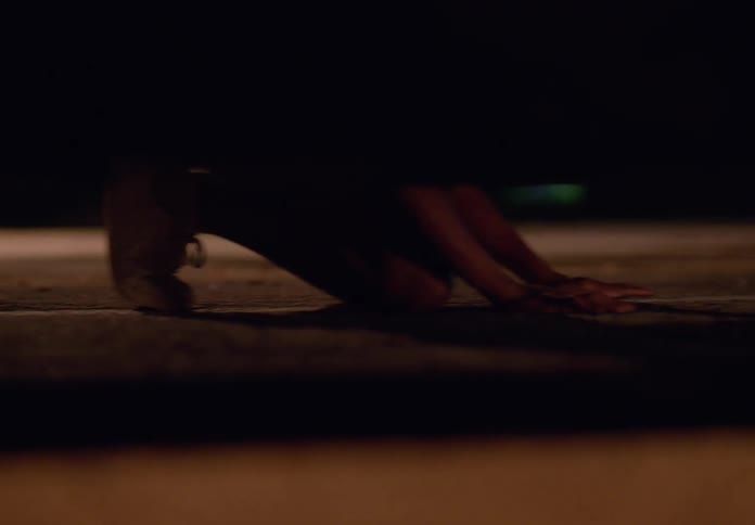 A pair of feet wearing lightcolored shoes walk along a dark rough surface at night the camera focuses closely on the ground with the upper part of the frame mostly dark showing only the lower legs and shoes in motion