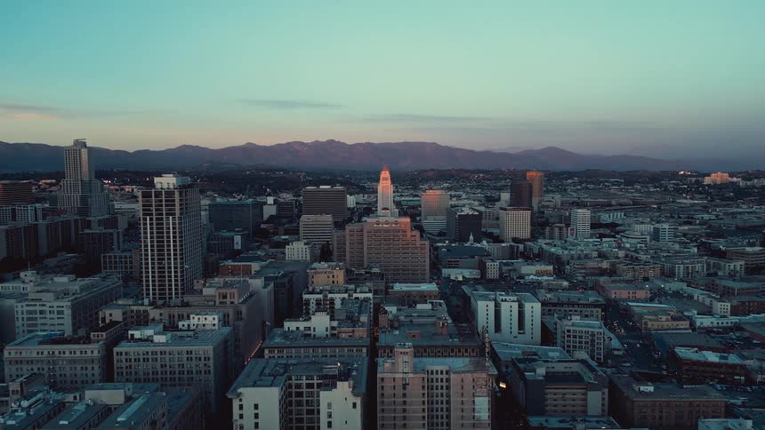 A dusky skyline frames a central tower glowing with orange lights set against distant mountains under a fading sky