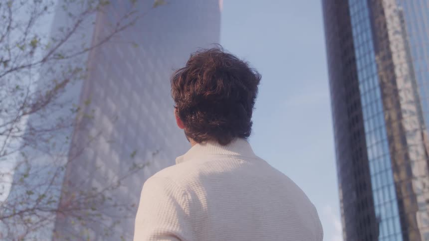 A man is standing and staring at a twintower city building at midday