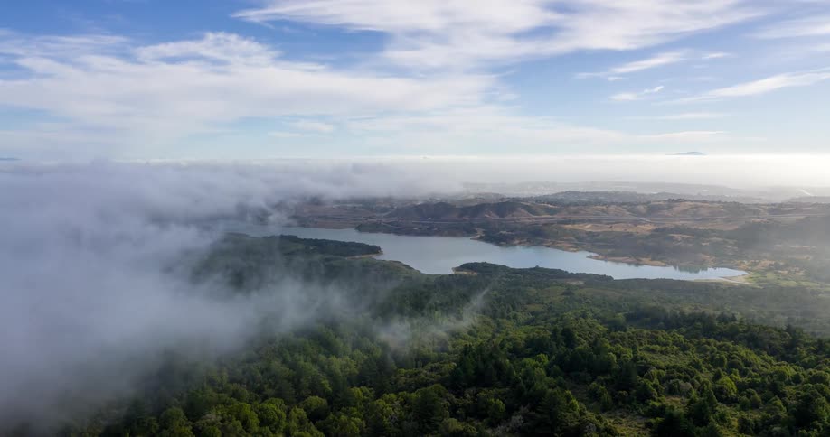 A winding river snakes through a dense forest under a layer of drifting mist