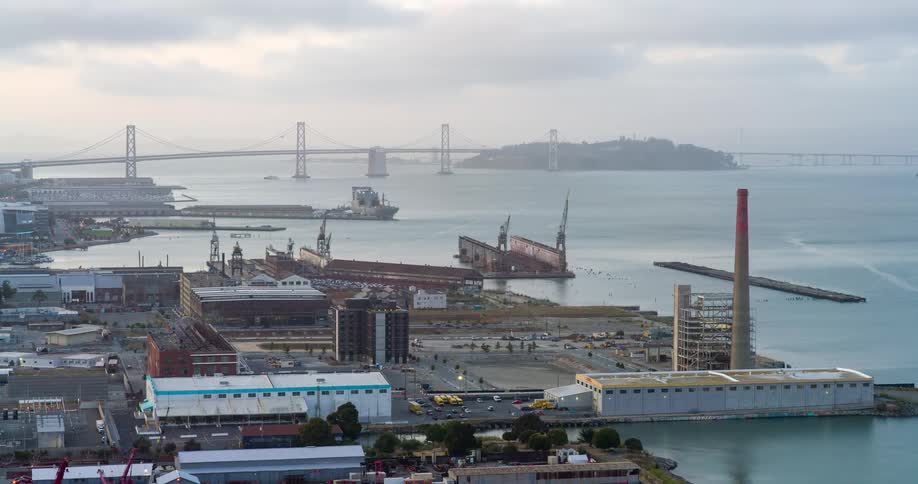 Aerial view of a port distribution center and waterfront factories with a bridge in the background
