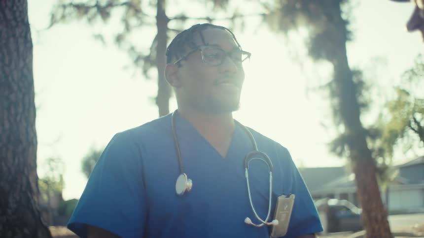 A healthcare worker talks to an older man outdoors in a warm suburban setting