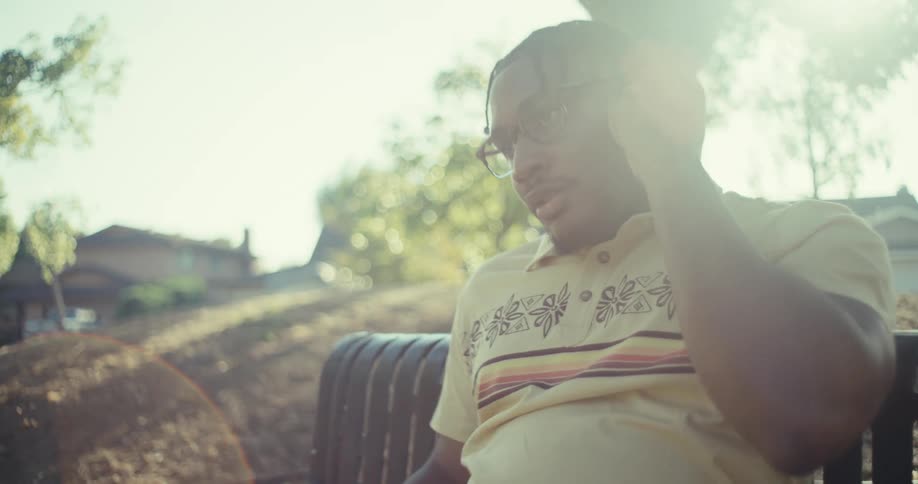 A man sits on a park bench talking on a call using wireless earbuds