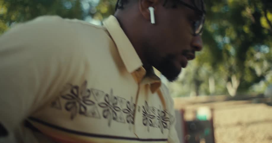 Close up of a young black man using his phone with airpods while sitting outdoors during daytime