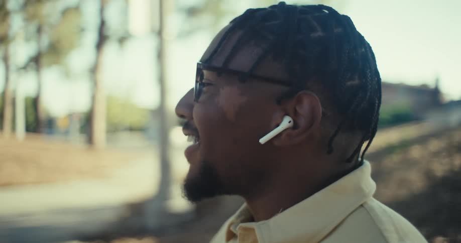 A man sits on a park bench listening to music on his smartphone and talking