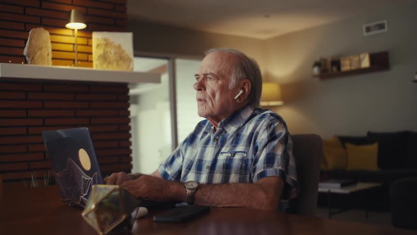 Elderly man using earbuds interacting with a laptop