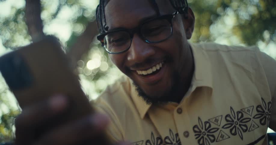 Man with happy expression using smartphone while sitting in outdoor environment with trees