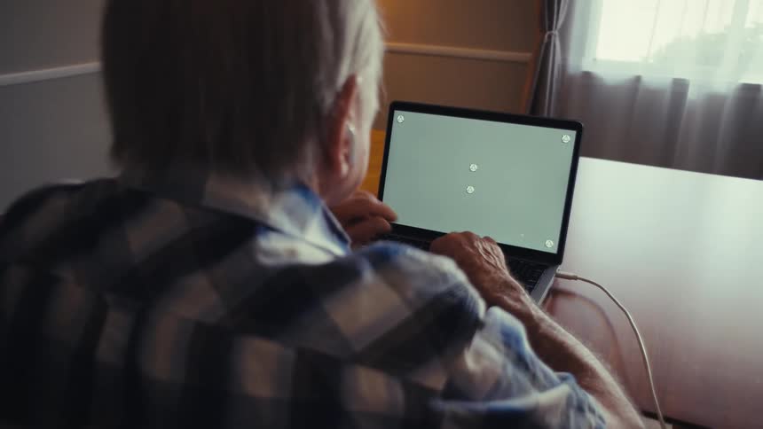 Elderly man sitting at a desk typing on a laptop