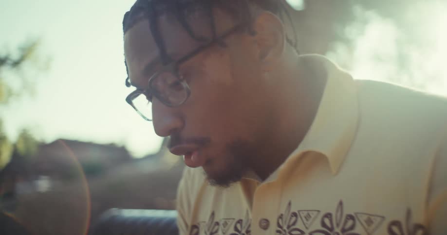 Young black man reacts emotionally as he uses his phone while sitting outdoors during daytime