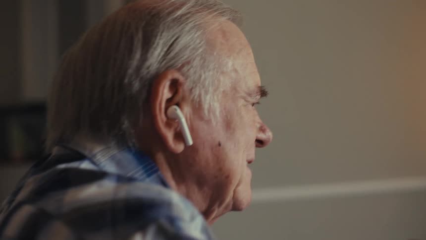 Close up of an elderly man using a laptop while sitting at a table in a living room during daytime