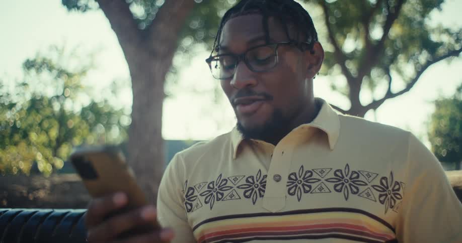Close up of a young black man using a phone while sitting outdoors during daytime