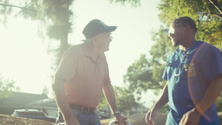 An elderly man with a walker shakes hands with a medical worker in scrubs