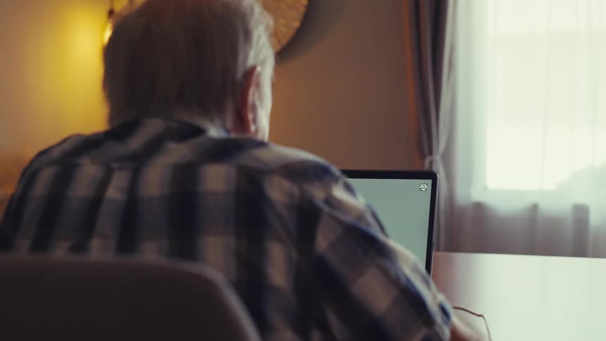 Elderly man sitting in front of an open laptop on the table