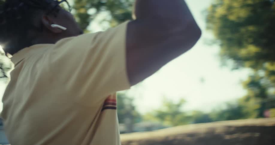 A man stands in a sunlit park laughing joyfully while looking at his phone during a video call