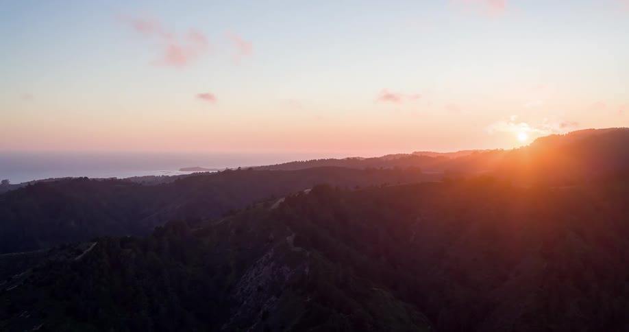 A golden sunset casts warm light over forested mountains and rolling hills