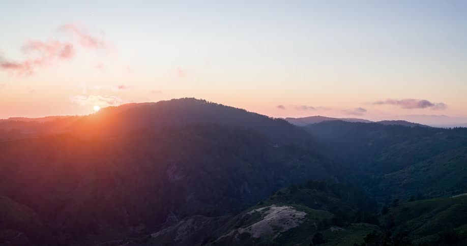 The sun sits behind a mountain range