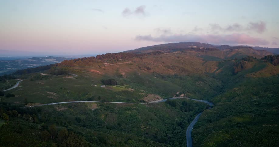 A winding road curves through rolling green hills at sunset