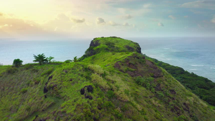 A lush green cliff juts out into the sea under a colorful sky