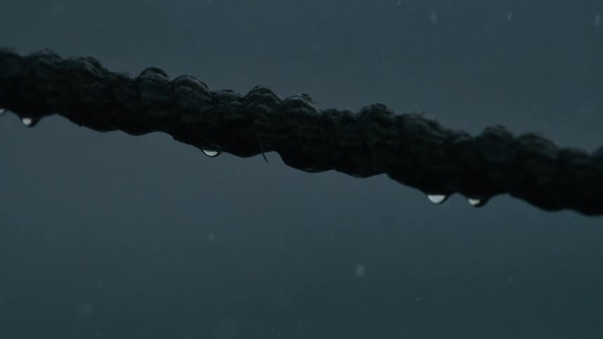 Clear water droplets cling to a dark textured rope against a muted gray rainy background