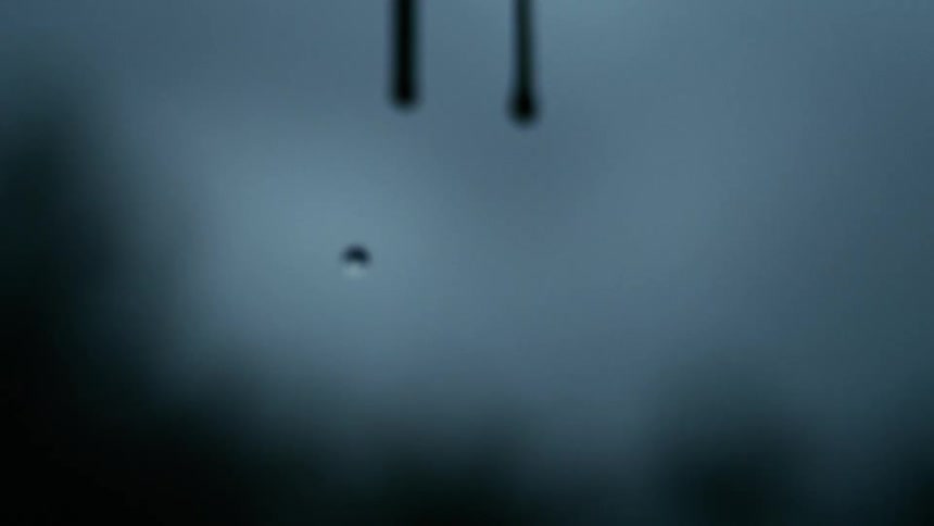 Raindrops fall down reflecting scattered light against a blurred backdrop