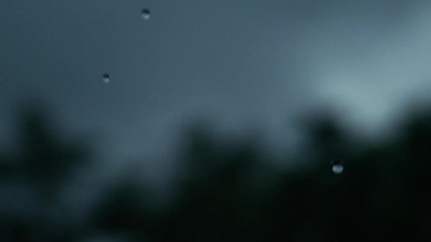 Raindrops falling against a dark overcast sky with tree silhouettes faintly visible in the distance