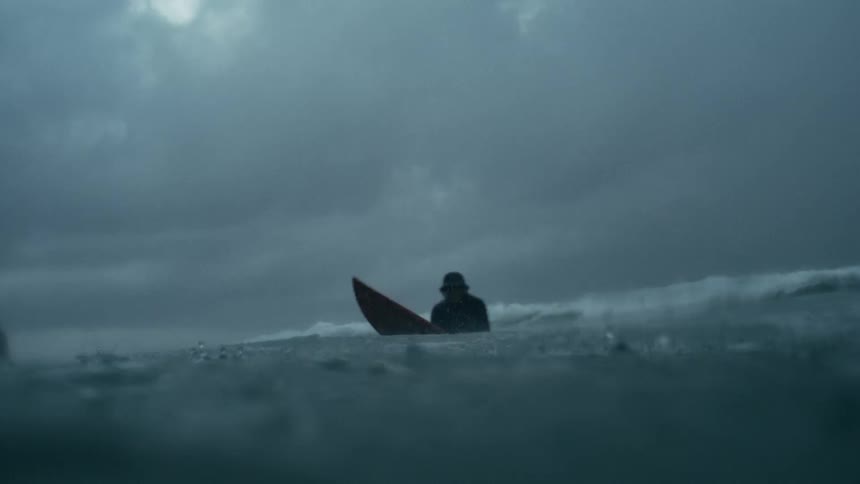 A lone surfer waits in dark choppy waters under a stormy sky