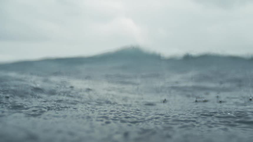 Rain falls over a choppy ocean surface under a cloudy sky