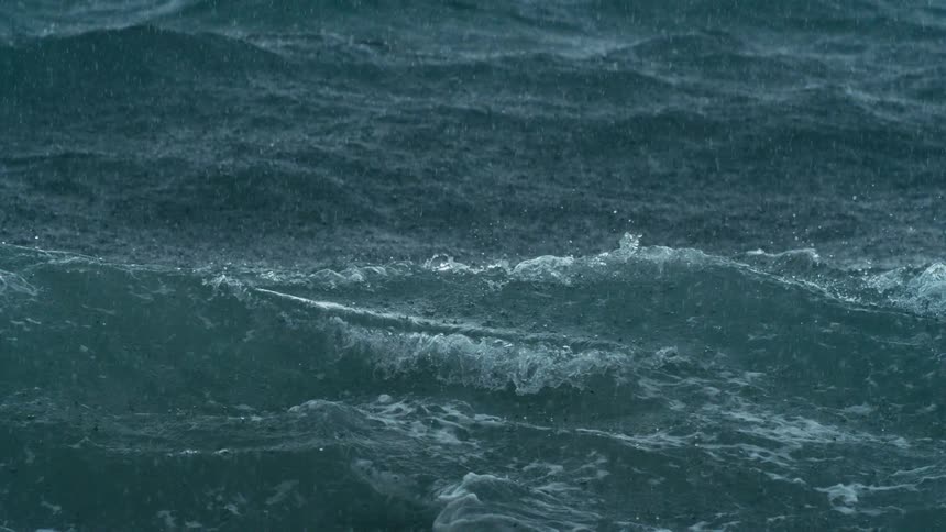Dark choppy ocean waves churn and splash under driving rain
