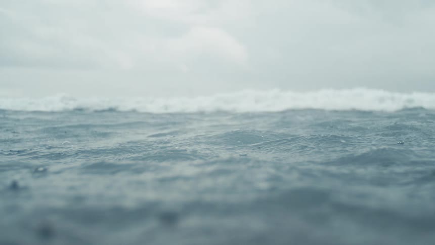 A lowangle shot of choppy ocean water with a large wave cresting in the distance under a cloudy sky the camera remains mostly still capturing the constant movement of the waves and the subtle shifts in the waters surface