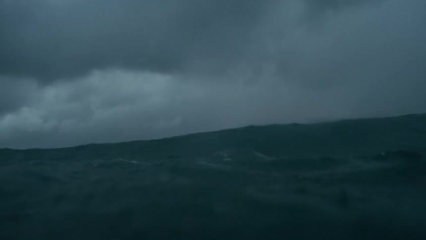 Dark turbulent ocean waves beneath a stormladen sky streaked with shifting gray clouds