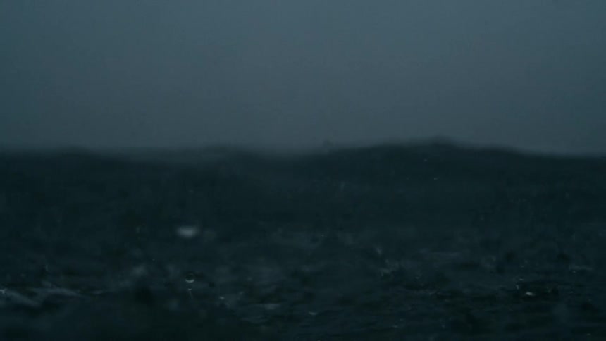 Dark turbulent ocean waves beneath a stormladen sky streaked with shifting gray clouds