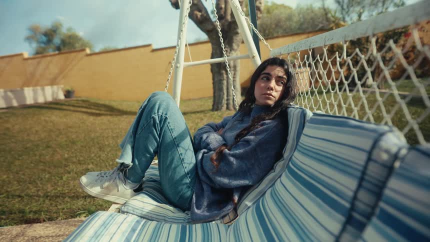 A girl relaxes alone on an outdoor swing in a quiet grassy yard
