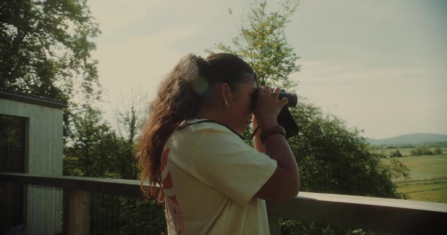 Young woman using binoculars and looking at a green landscape with mountains