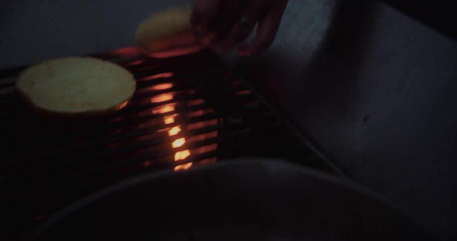 Hand putting hamburger bun on the grill