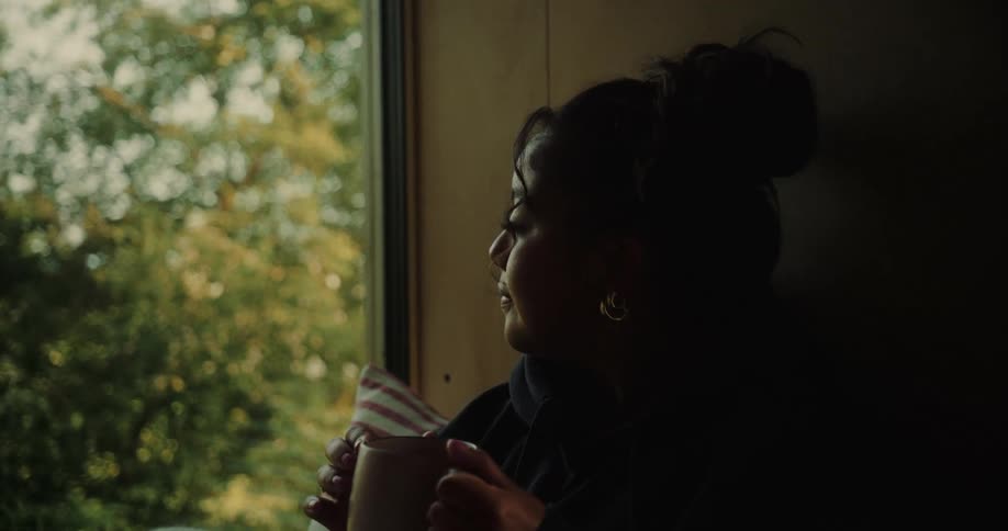 Woman holding a cup sitting on a window sill