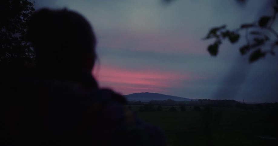 Silhouette of a person in the foreground and in the background mountains in a field with a purple sky