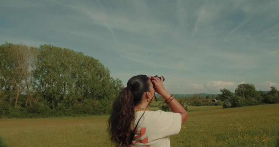 The woman is using binoculars on the field