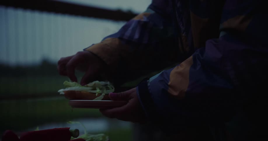 Woman in an outdoor setting assembling a sandwich with salad