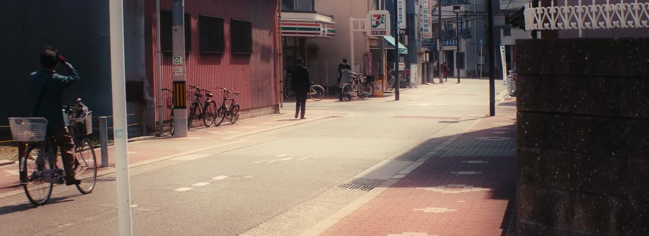 Pedestrians and cyclists move along a hazy city street in Japan during the daytime