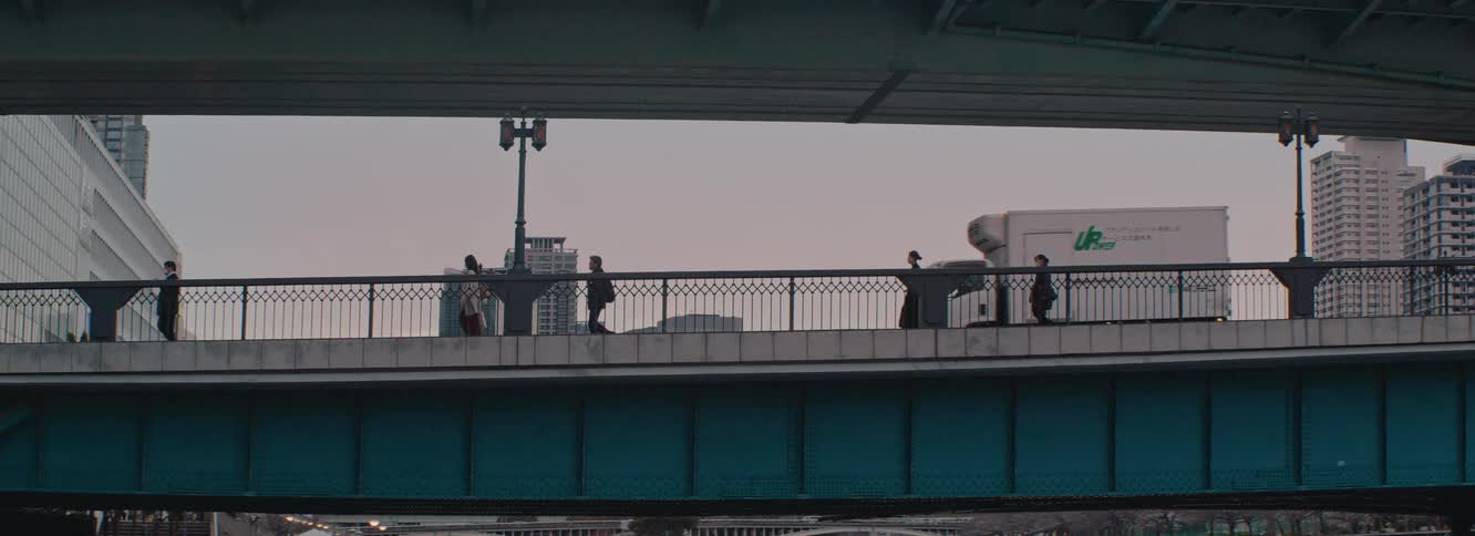 People walk across a bridge at sunset with silhouetted buildings in the background and reflected light on the water below in Osaka Japan