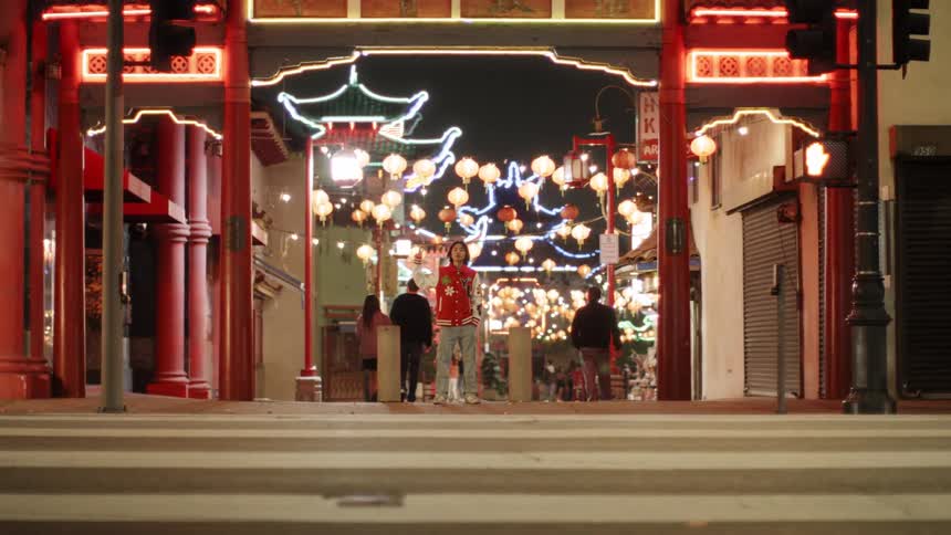 A teenager stands on the side of the road at night waiting to cross a busy street